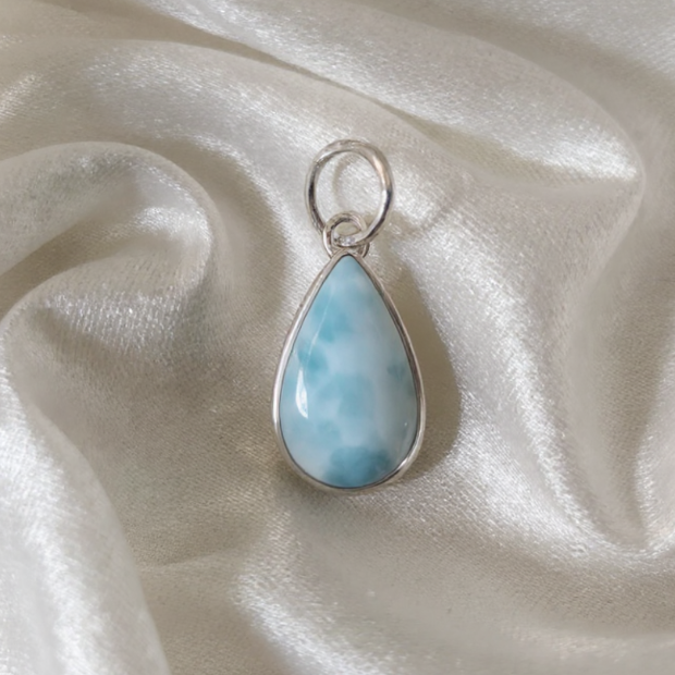 Teardrop-shaped larimar pendant on a white satin background