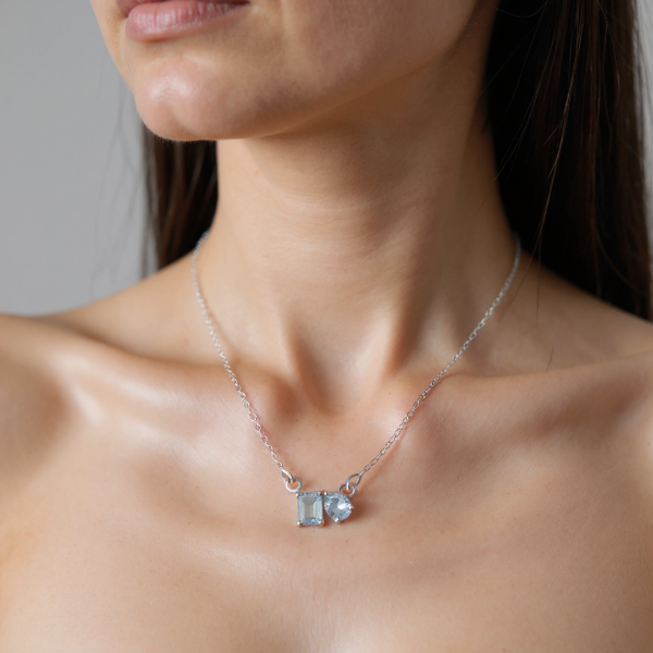 Close-up of a woman wearing a silver necklace with a pendant featuring two blue gemstones.