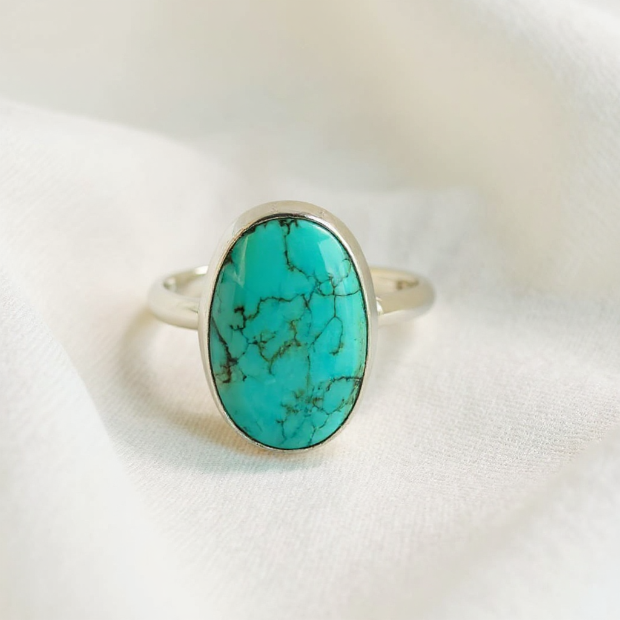 Turquoise ring with silver band on a white fabric background
