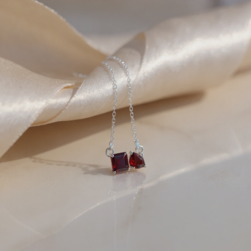 Silver necklace with red gemstones on a beige satin background