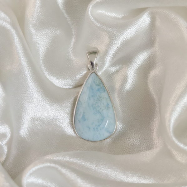 Teardrop-shaped larimar pendant on a silver chain against a satin background