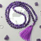 Purple beaded necklace with a tassel on a light gray background