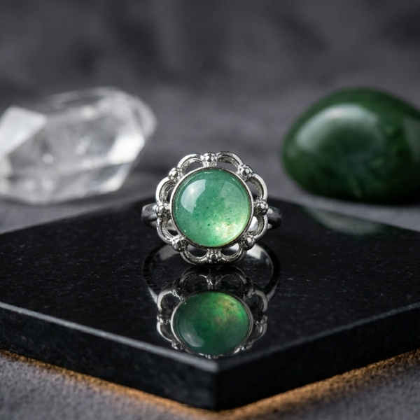 Green gemstone ring with silver band on a dark surface
