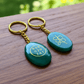 Two green aventurine keychains with gold accents on a wooden surface