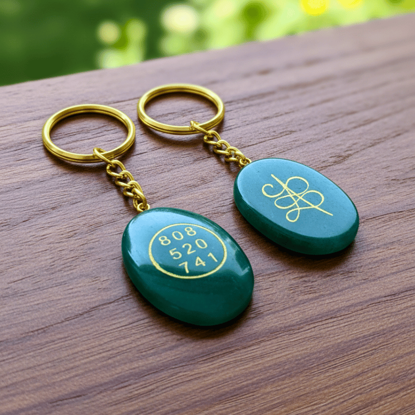 Two green aventurine keychains with gold accents on a wooden surface
