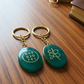 Two green aventurine keychains with gold text on a wooden surface