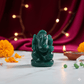 Green Ganesha statue on a table with marigold flowers and a lit candle in the background.