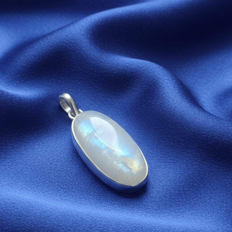 Silver pendant with a rainbow moonstone on a blue fabric background