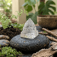 Crystal pyramid on a black stone with plants and wooden elements in the background