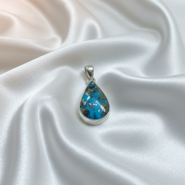 Teardrop-shaped pendant with blue stone on a white satin background