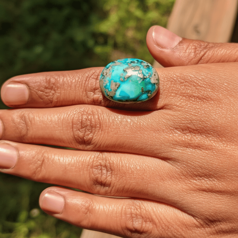 Hand wearing a turquoise ring with a natural background